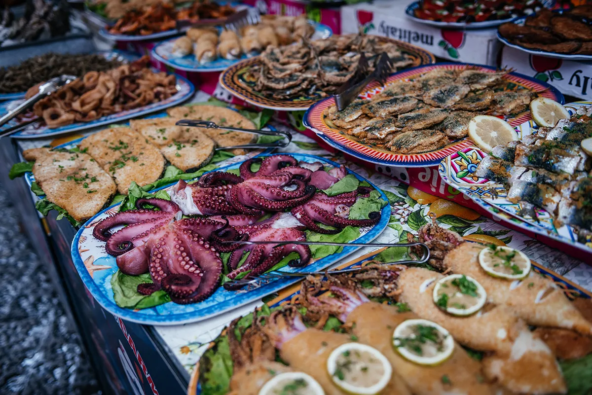 Platters of octopus, swordfish and prawns on painted trays at a Palermo market stall