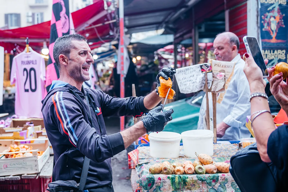 A Ballarò market vendor laughing as he serves a customer