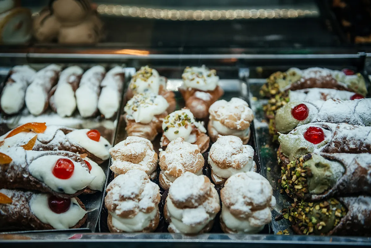 A pastry counter of cannoli and ricotta pastries topped with candied cherries