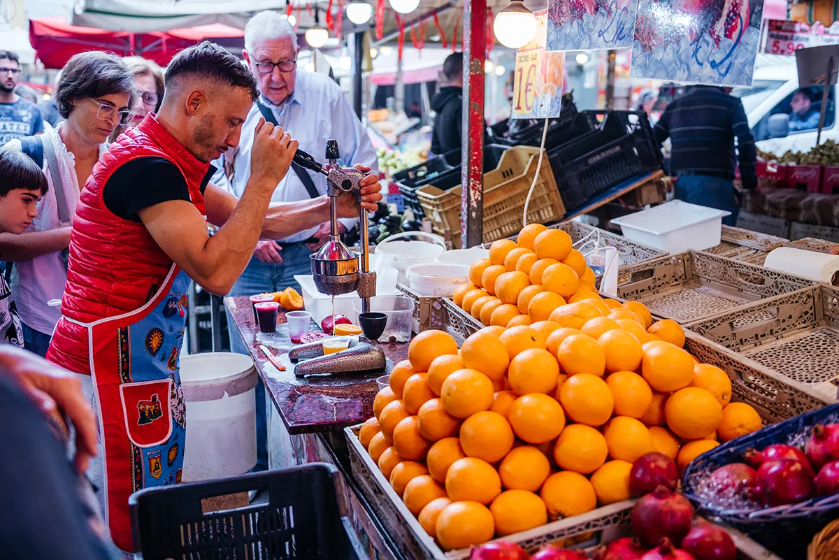 A vendor squeezing fresh orange juice behind a pyramid of oranges