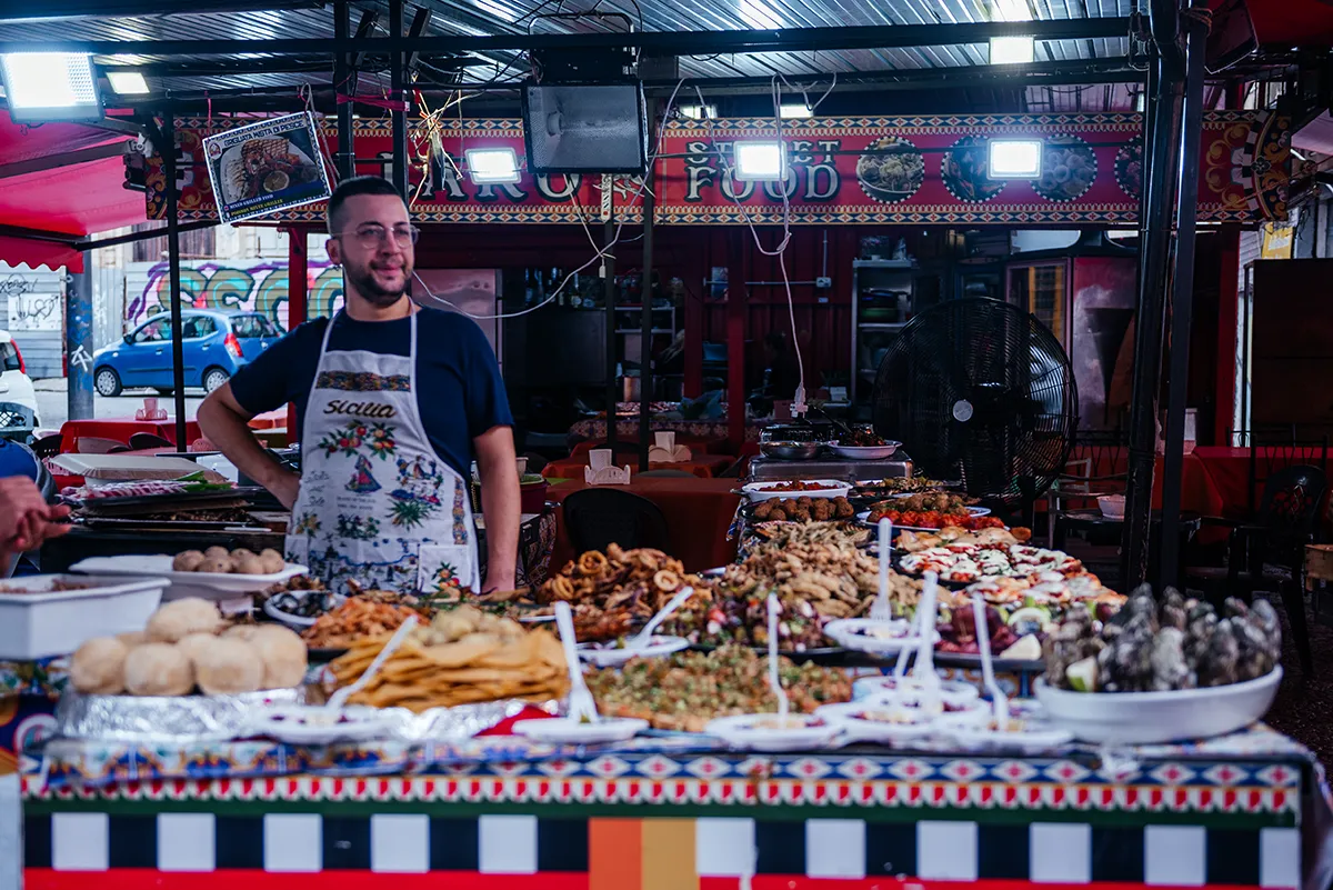 A vendor behind a long street food counter in a Palermo market