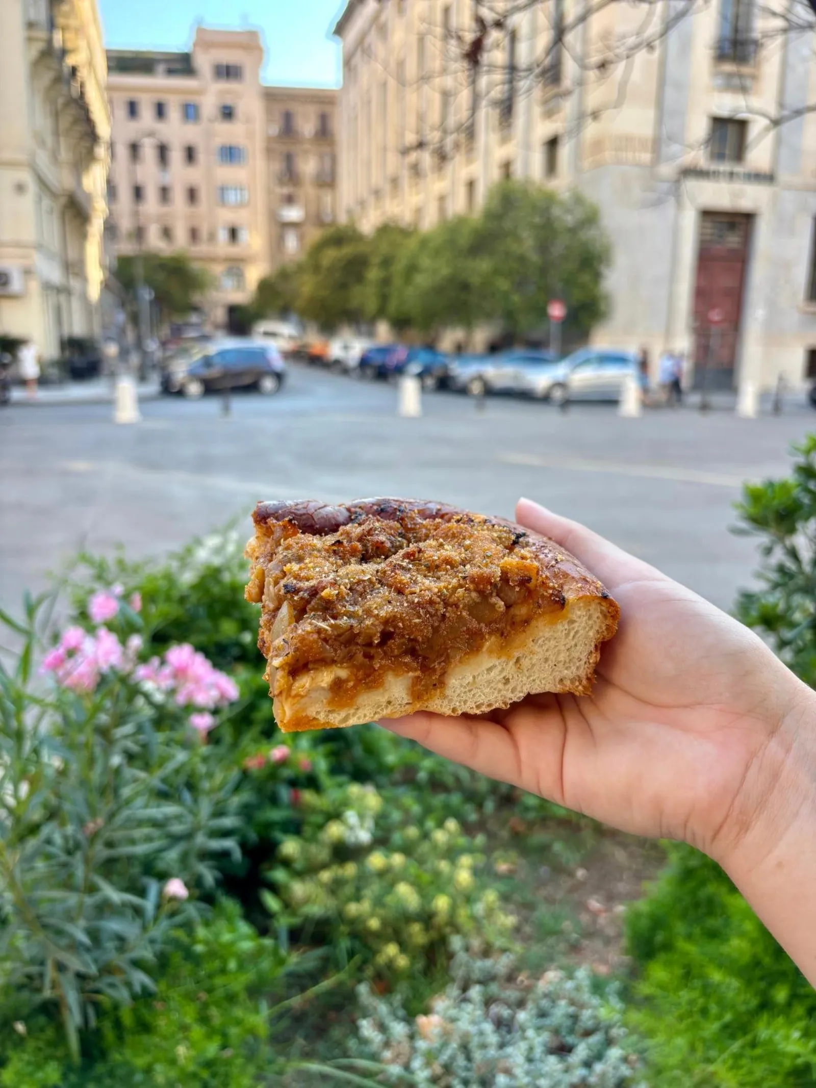 A slice of sfincione held up in a Palermo street