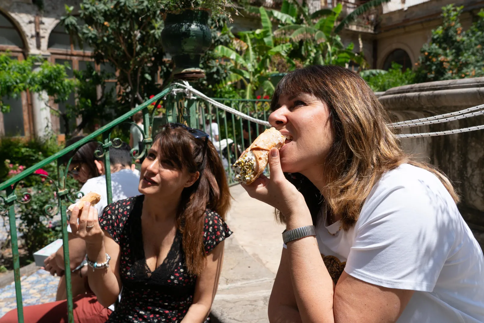 Two guests eating street food on the steps of a garden square