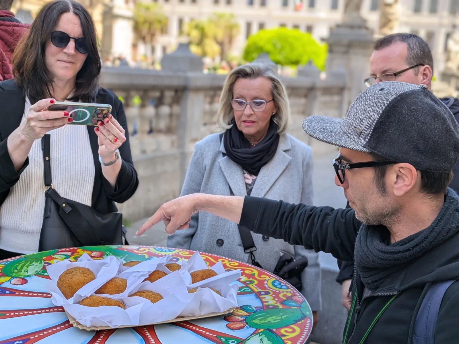 The guide points out arancine on a painted Sicilian cart table