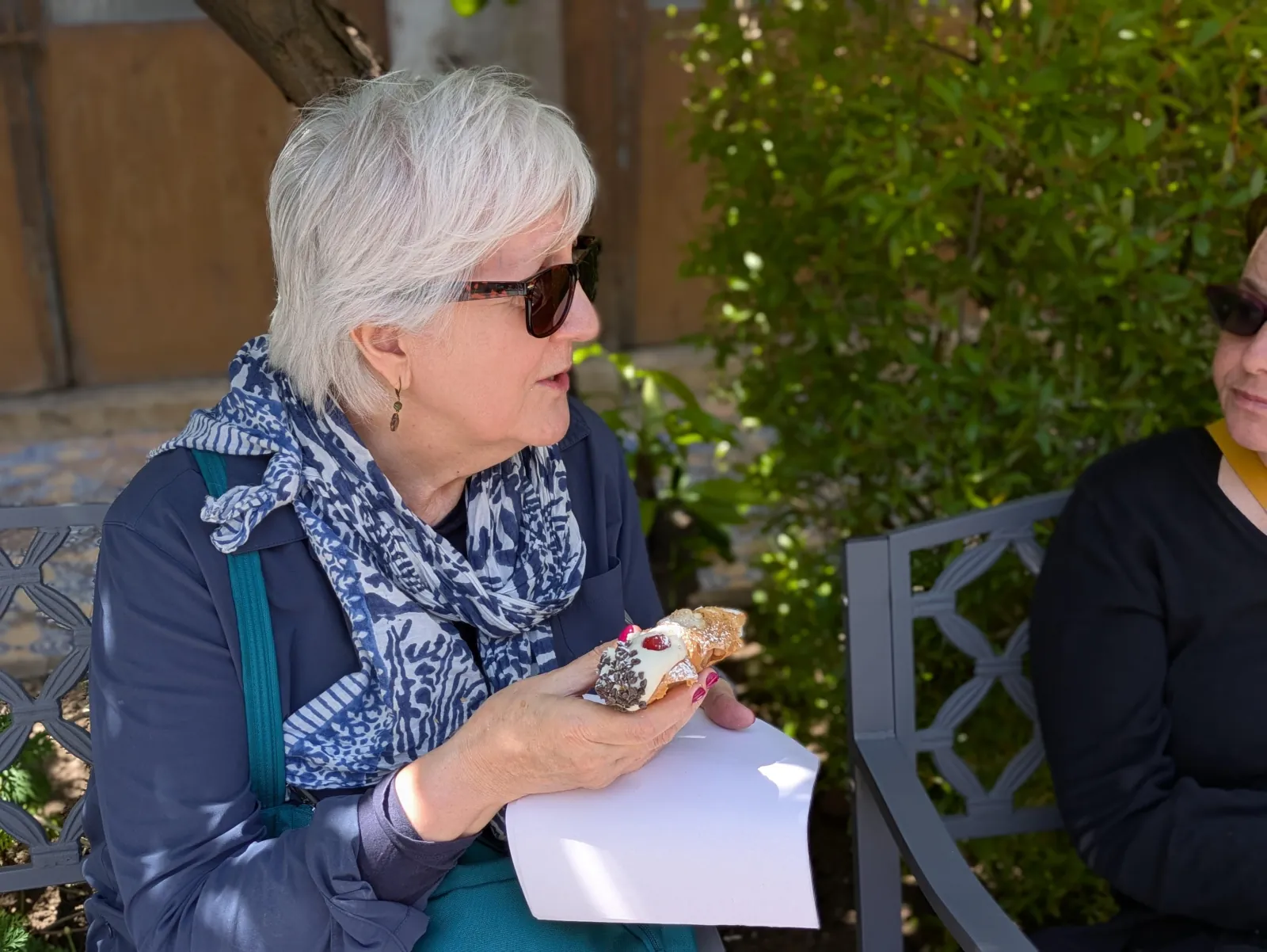 A guest with a cannolo in a shaded courtyard