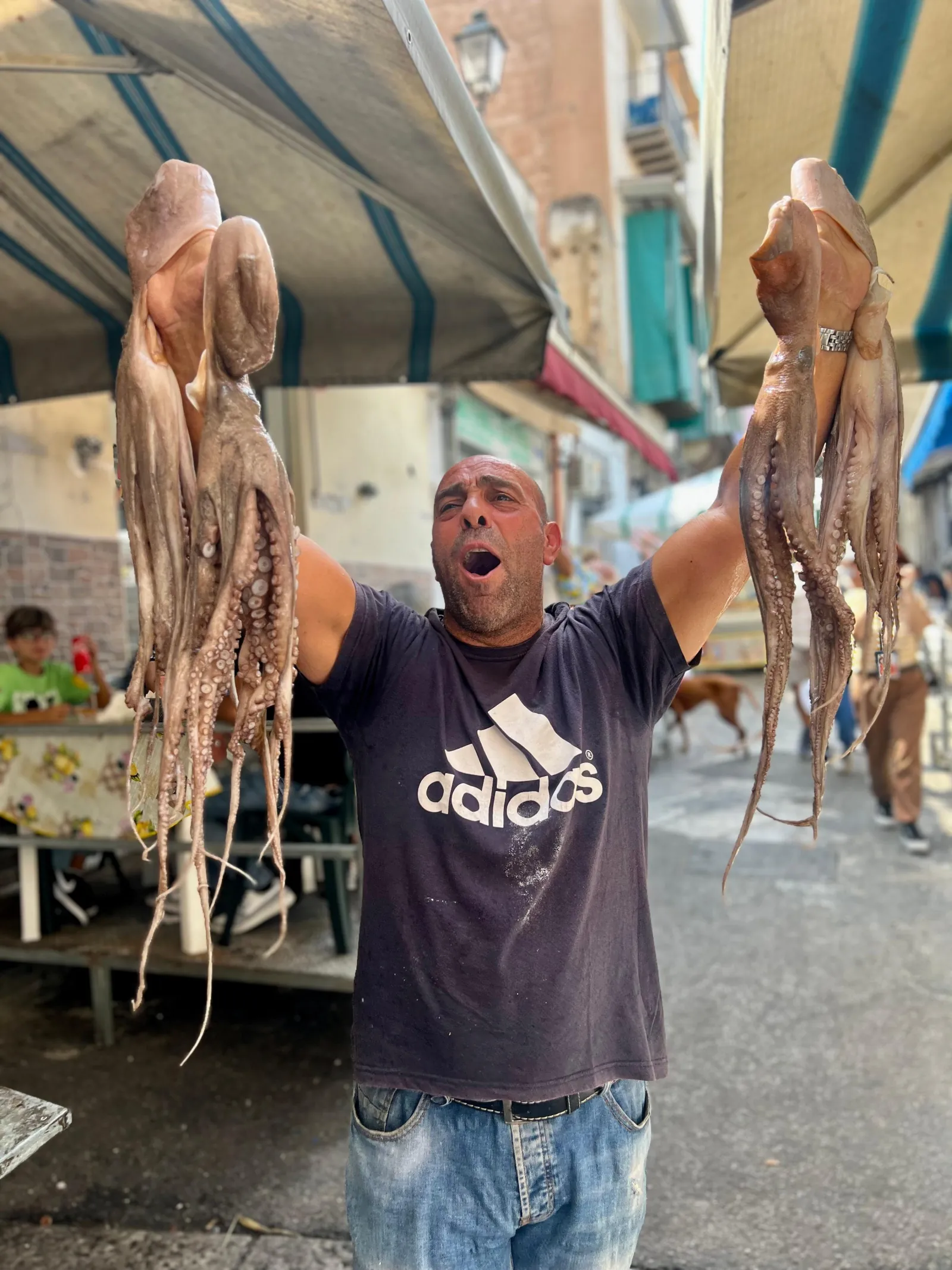 A fishmonger holds up two octopus at a market stall