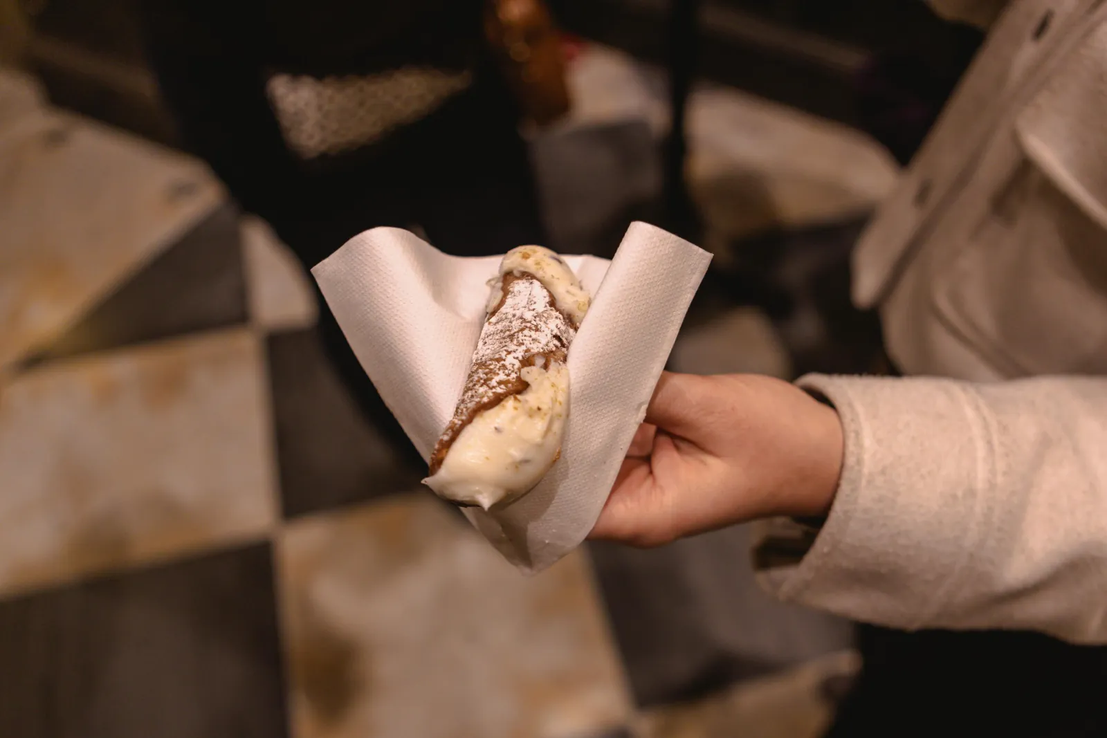 A cannolo handed over in a paper napkin