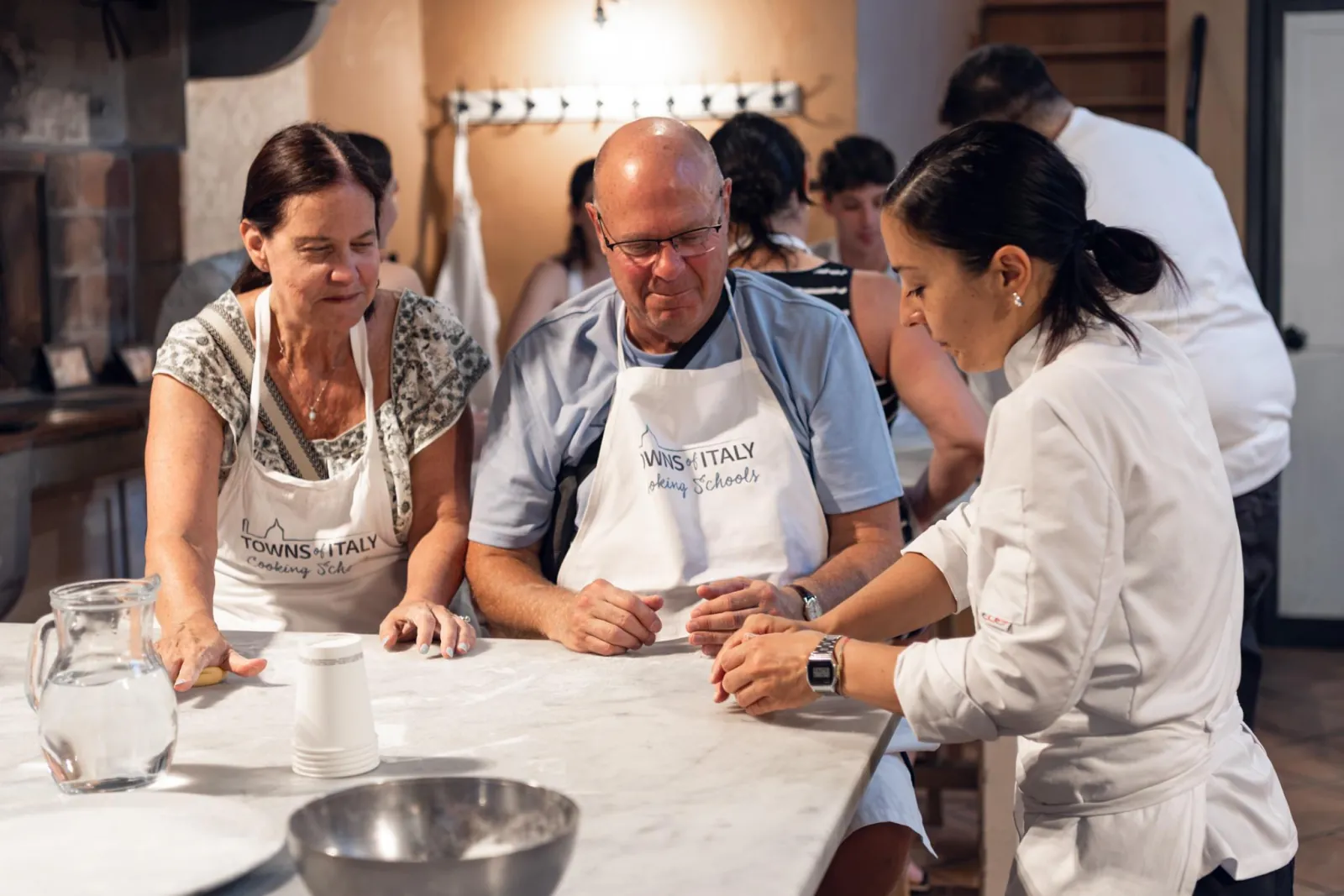 The chef guides two guests through a pasta step